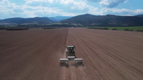 toma aérea trasera de un tractor tirando de rodillos pesados a un campo grande y plano, plataforma rodante en