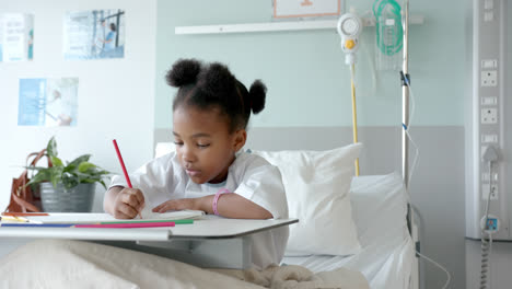 Niña-Afroamericana-Dibujando-En-Un-Cuaderno-En-La-Cama-De-Un-Hospital,-En-Cámara-Lenta