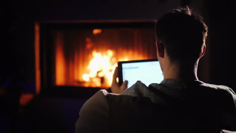 silhouette of a man uses a tablet sits in the twilight by the fireplace