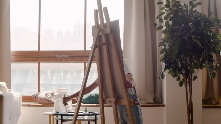 Ragazza bionda che dipinge il suo disegno con un pennello su un cavalletto nel soggiorno di casa.