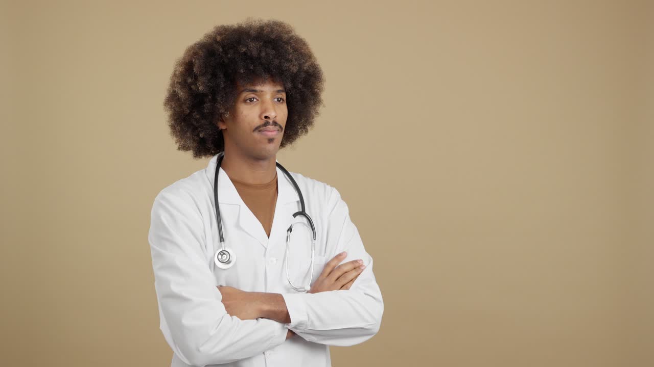 A male doctor with an afro hairstyle and stethoscope stands with arms crossed
