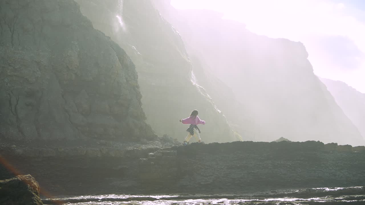 Young Woman Exploring Rocky Coastline Cliffs in Bright Sunlight