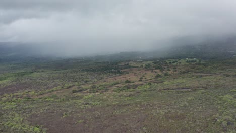 Wide-aerial-panning-shot-of-the-active-volcano-Hualālai,-as-it-disappears-into-the-clouds-on-the-Big-Island-of-Hawai'i