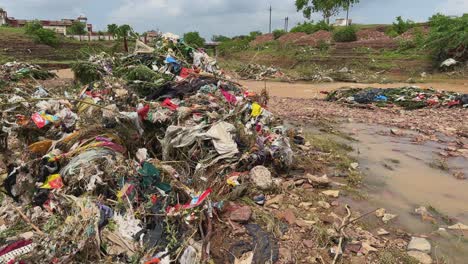 a heaps of garbage entangled in bushes and vegetation along the river floodplain, plastic bags, torn clothes, packaging materials, and organic waste carried and deposited by recent floodwaters