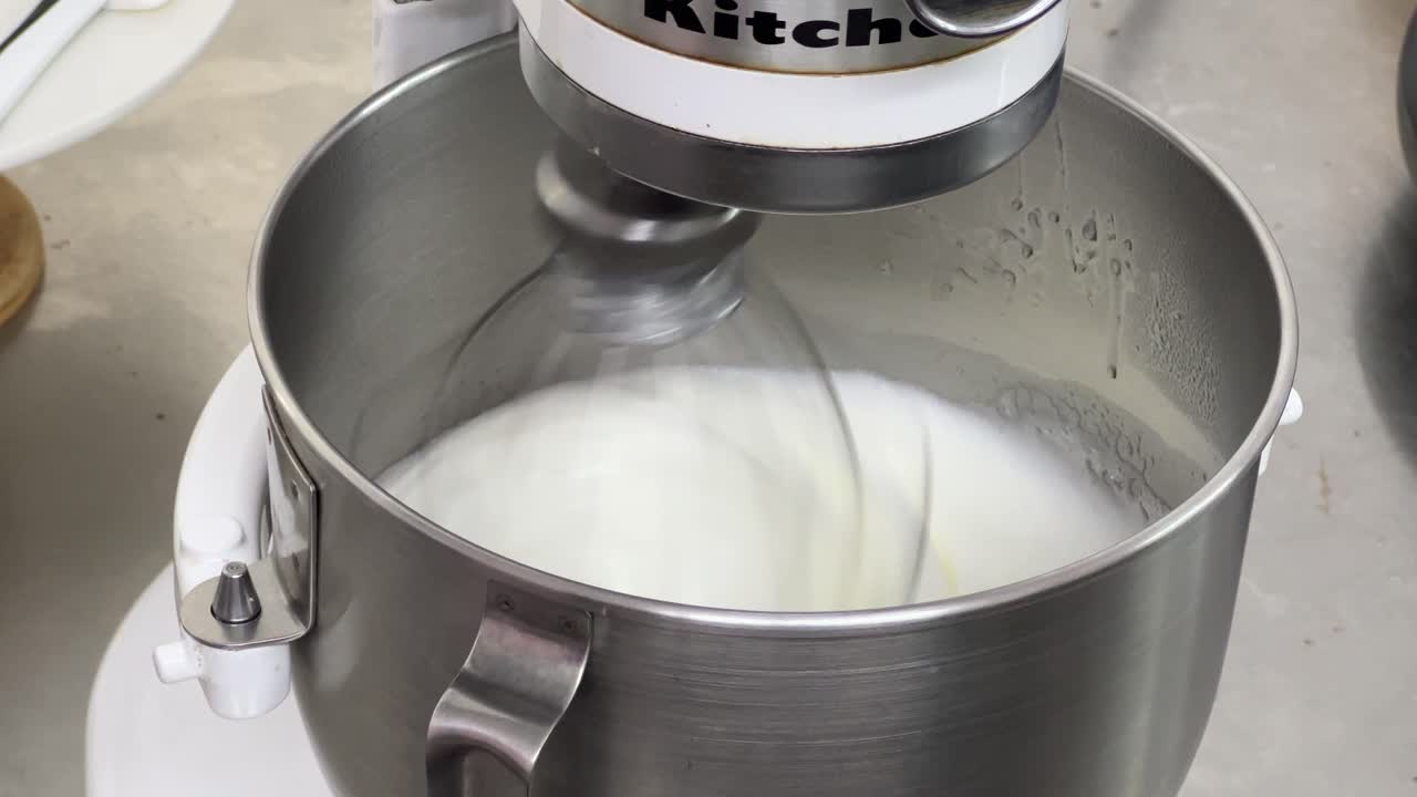 pastelería de crema de mantequilla de merengue suizo esponjoso y suave en progreso, primer plano de una batidora eléctrica mezclando y batiendo la clara de huevo y el azúcar hasta que es un pico brillante y un pico rígido