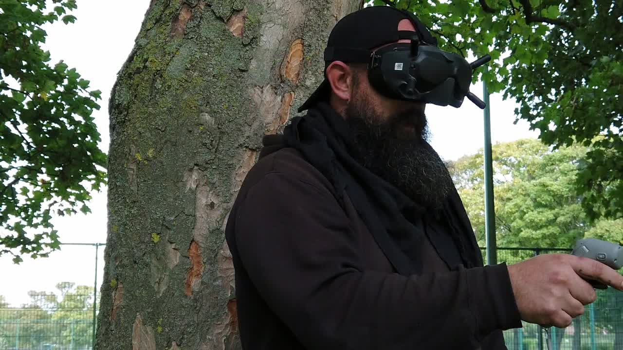hombre barbudo con gafas fpv inalámbricas que controlan drones en el parque con joystick de movimiento