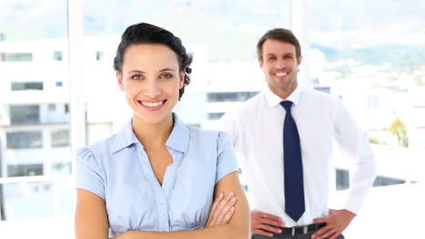 mujer de negocios sonriendo a la cámara con un colega detrás de ella