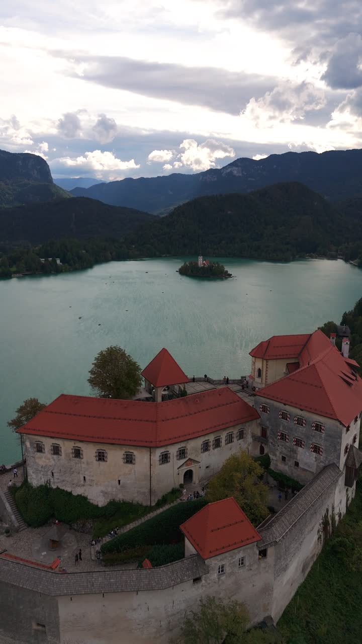 Vista aerea verticale con drone del castello di Bled con vista sul lago di Bled in Slovenia. La carrellata in avanti rivela l'architettura storica, le acque turchesi e le colline boscose