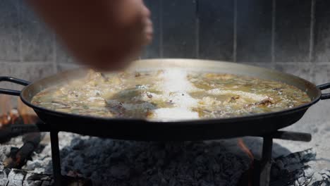 adding rice to paella being cooked over an open fire