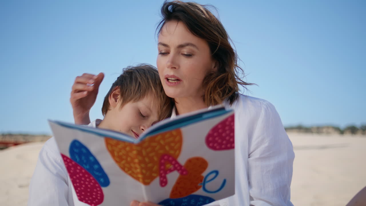 Mom child enjoying book sitting sandy beach summer day closeup. Relaxed boy