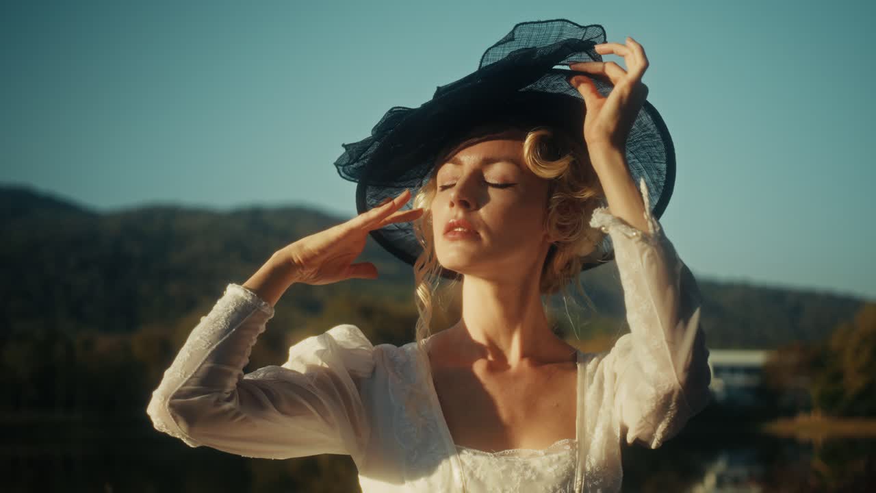 Donna elegante con abito e cappello vintage che posa all'aperto durante l'ora d'oro