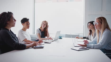 Equipo-De-Jóvenes-Empresarias-Con-Computadoras-Portátiles-Y-Tabletas-Reunidas-Alrededor-De-Una-Mesa-En-Un-Espacio-De-Trabajo-Moderno