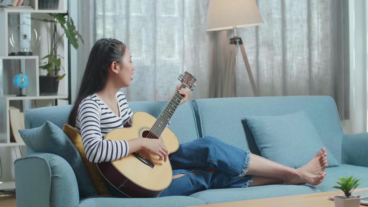 소파 에서 어쿠스틱 기타 를 연주 하는 여자