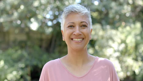 Retrato-De-Una-Feliz-Mujer-Birracial-Mayor-Con-El-Pelo-Corto-En-Un-Jardín-Soleado-En-Casa,-Cámara-Lenta