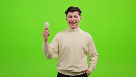 the man is standing and looking at the camera. he is picking up the light bulb and looks at it. he is smiling. he is standing on a green background. green screen. 4k