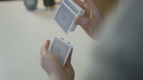 man shuffles deck of cards for a magic trick in his home living room over shoulder view