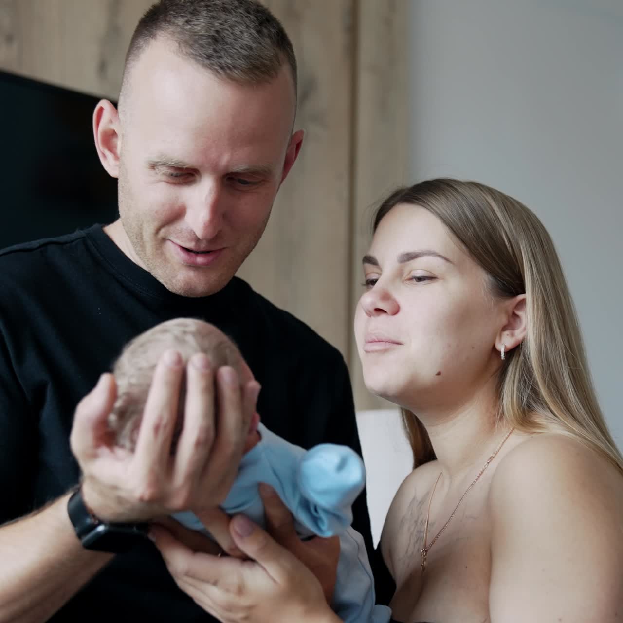 Mid-aged man holding his newborn baby carefully. Long-haired woman stands beside supporting child's back