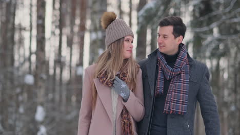 Young-married-couple-in-love-walking-in-the-winter-forest.-A-man-and-a-woman-look-at-each-other-laughing-and-smiling-in-slow-motion.-Valentine's-Day-love-story.