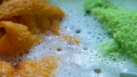 close-up of orange and green cloths soaking in soapy water