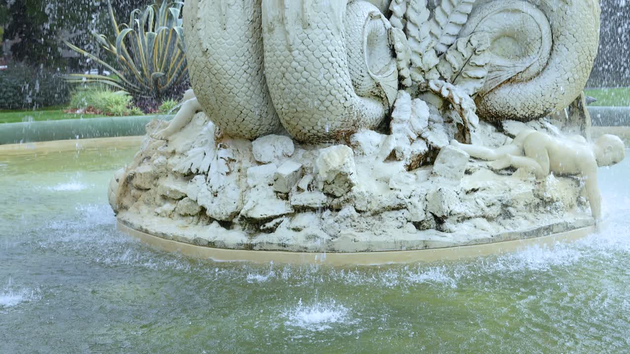 una vista detallada de una fuente decorativa con esculturas intrincadas y agua corriente en un entorno de parque exuberante