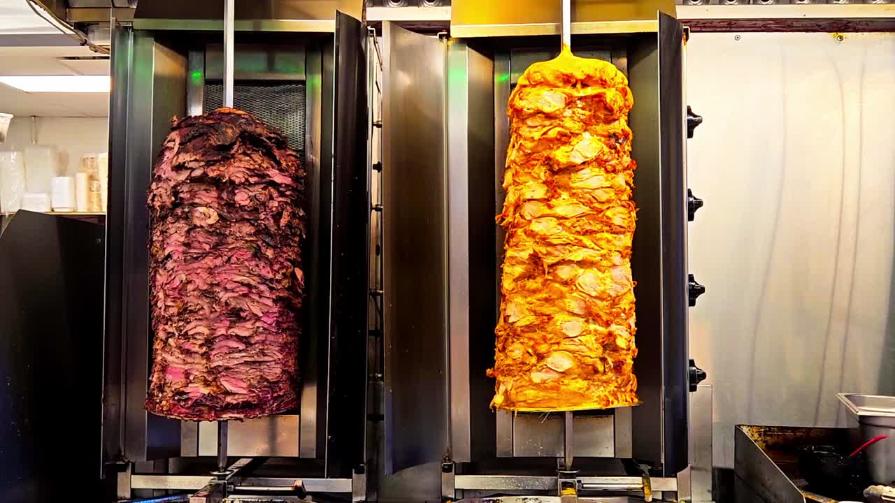 Tenderloin beef steaks are cooking on a rotisserie vertical electric BBQ at a restaurant along with perfectly marinated chicken chest cutlets ready to be served