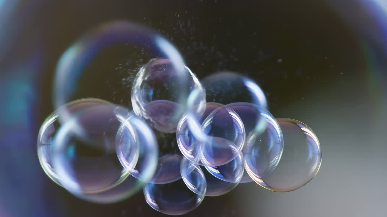 Gruppo di bolle di sapone iridescenti che fluttuano in un primo piano macro cinematografico al rallentatore, sfere trasparenti riflettono