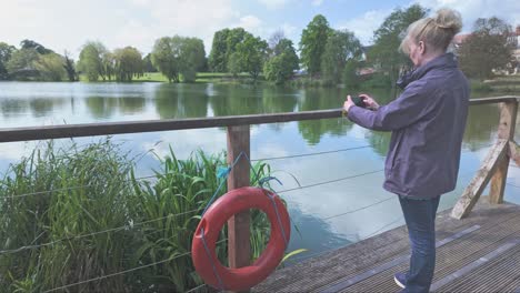 female tourist takes snapshot of diss park lake from boardwalk with lifebouy ring