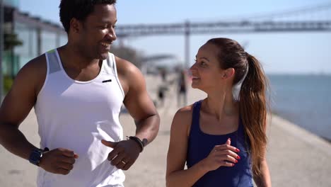 Happy-sporty-young-couple-jogging-along-embankment