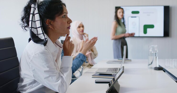 Team femminile che reagisce al presentatore che indica una slide in ufficio, donna in primo piano a sinistra che applaude