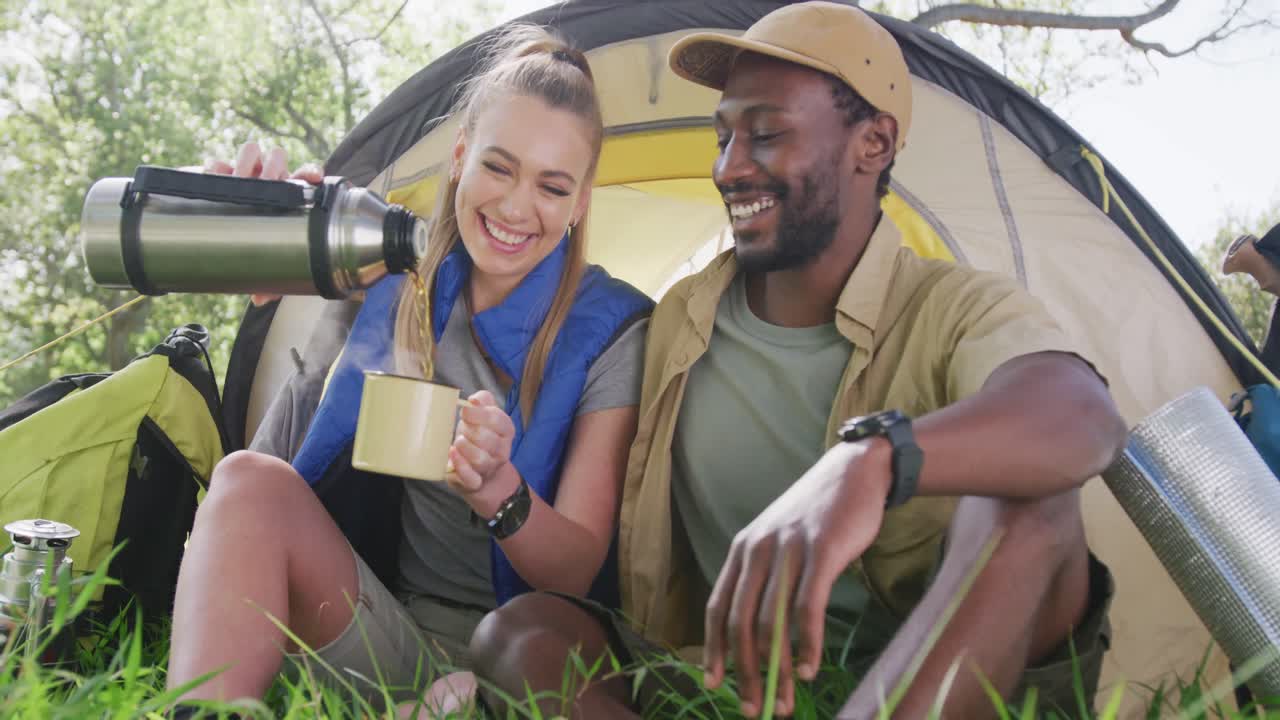 Coppia felice e diversificata che fa campeggio e beve tè nel parco, al rallentatore