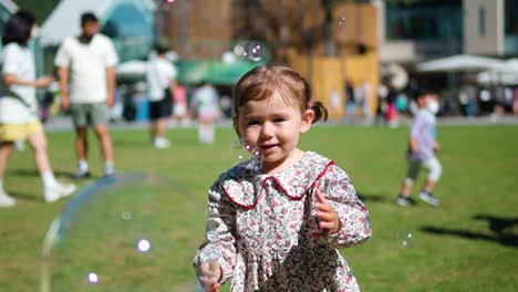 smiling little baby girl smashing bubbles with hands in a playground on summer day