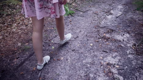 crop view of a girl wearing dress and white sneakers walking in forest