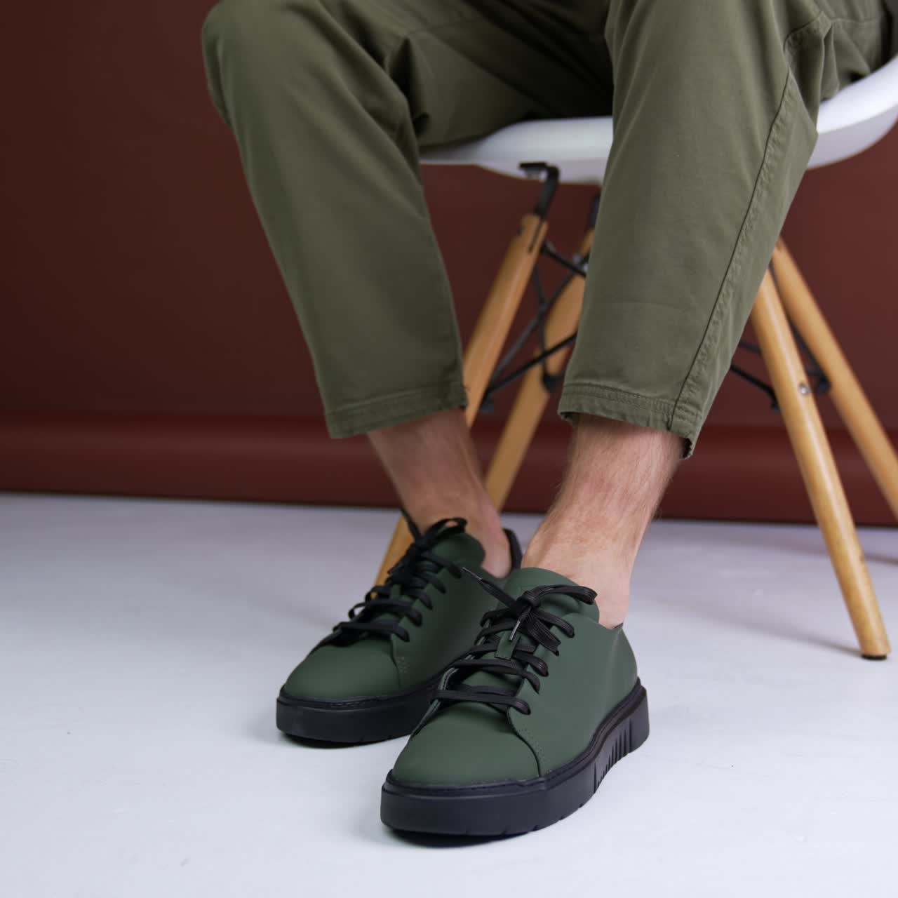 Man wears khaki jeans and khaki sneakers. model sits on the chair in studio demonstrating his stylish footwear