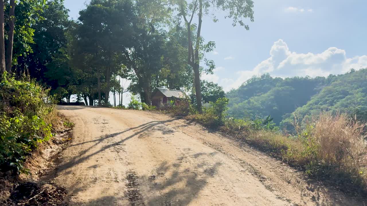 A winding dirt road through Phuket's verdant landscape under bright daylight, surrounded by trees and hills, creating a serene atmosphere