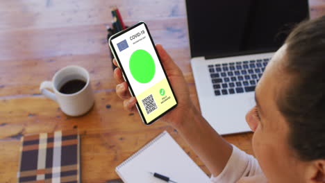 mujer en el escritorio con un teléfono inteligente con certificado de vacunación contra la covid, bandera de la ue y código qr en la pantalla