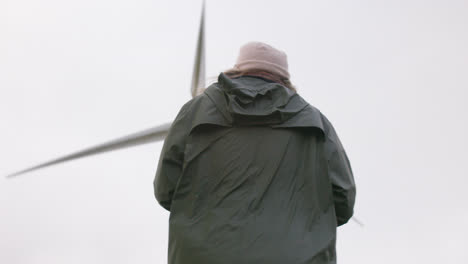 female walks with wind turbine in background