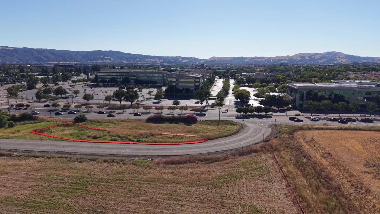 Un video drone mostra il quartiere degli affari di Dublino, California, con edifici per uffici, ampi parcheggi, strade sgombre, campi dorati e dolci colline in una giornata di sole.