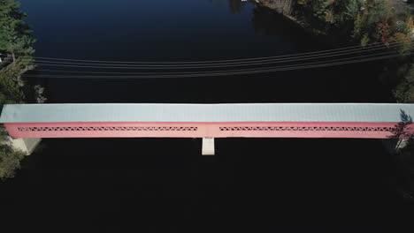 an aerial drone view tilting up to reveal a red and gray covered walking bridge across a river