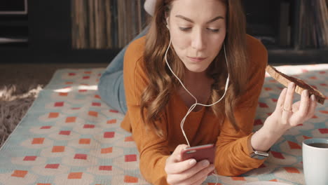 beautiful woman eating snack at home using smartphone listening to music