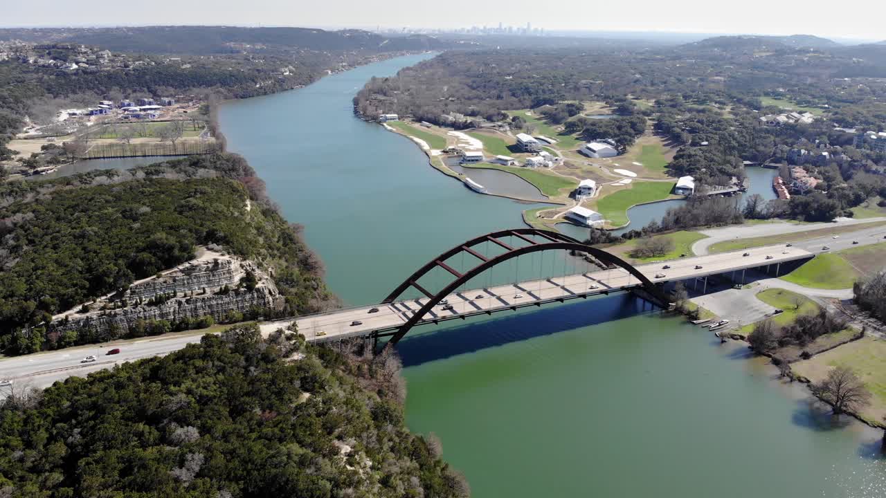 Aerial Austin Pennybacker Bridge - pulling up - away getting closer to the river, complete view of the bridge, overlook areas, and Austin skyline in far distance