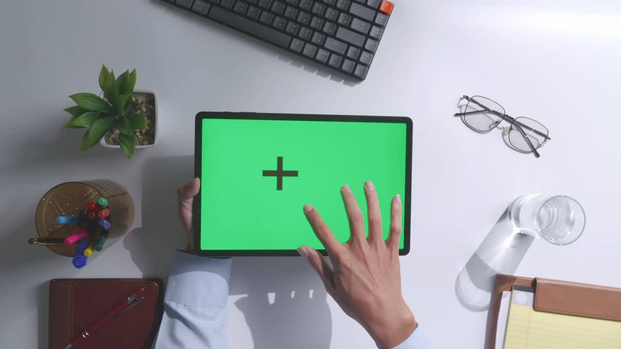 vista de arriba hacia abajo de una computadora portátil con pantalla verde simulada pantalla chromakey en un escritorio de oficina de madera al lado de la libreta con bolígrafos, gafas y un vaso de agua.