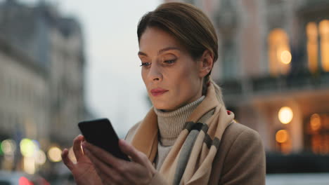 Vista-De-Cerca-De-Una-Joven-Empresaria-Caucásica-Enviando-Mensajes-De-Texto-A-Su-Smartphone-En-La-Calle-Con-Luces-De-La-Ciudad-En-El-Fondo