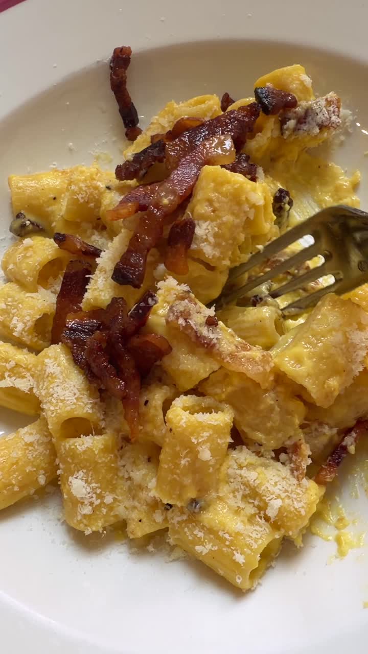 Primo piano di pasta alla carbonara cremosa con pancetta croccante e formaggio grattugiato.