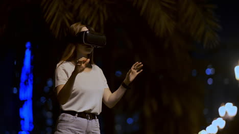 A-young-woman-in-virtual-reality-glasses-in-the-night-city-moves-her-hands-mastering-the-application-interface.-VR-technologies-of-the-future-in-everyday-life.-Virtual-reality-games