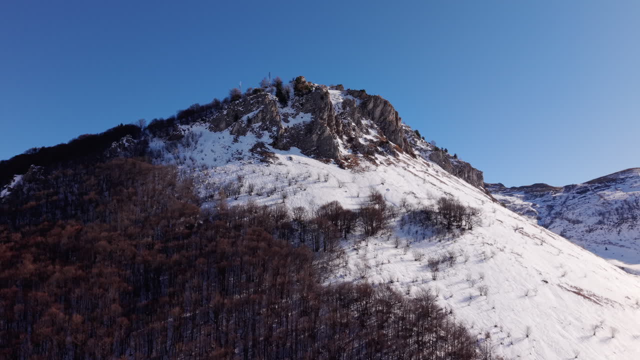 Ripresa aerea invernale della cima di una montagna sulle Alpi italiane con scogliere rocciose sotto un cielo blu