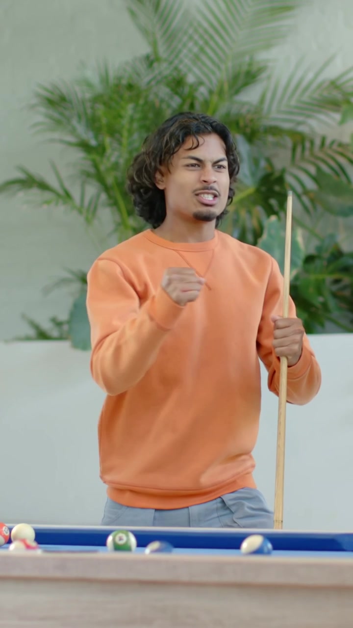 Vertical video: Lining up shot man in orange top holding cue aiming ball at pool table calling shot