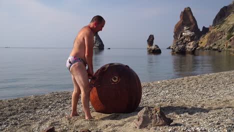 hombre haciendo ejercicio al aire libre cerca de una vieja mina marina flotante oxidada en la playa con orilla rocosa y fondo marino. estilo de vida saludable, contaminación, protección de la naturaleza, concepto de guerra y paz