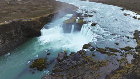 tourists visiting the godafoss waterfall with rocky cliffs in iceland