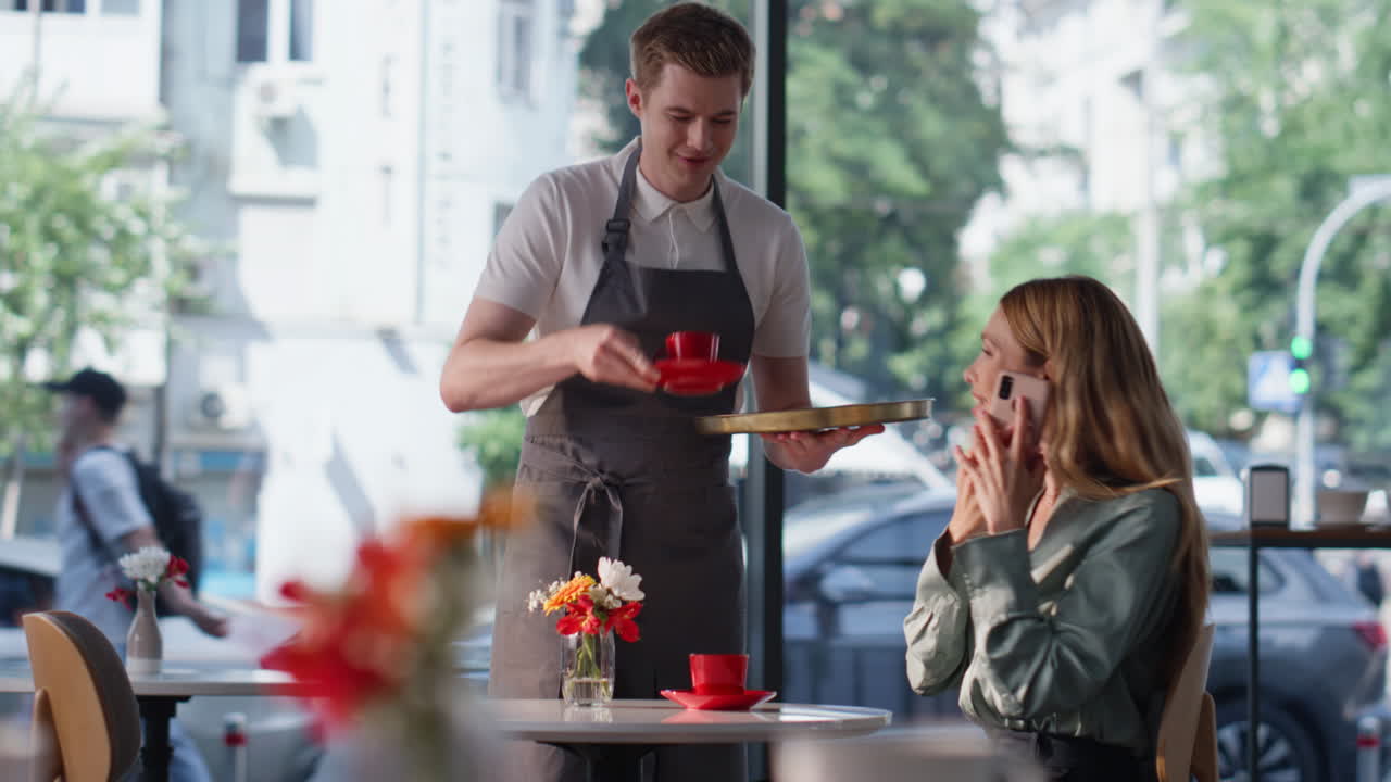 Joyful blonde talking cellphone sitting restaurant table. Smiling woman calling