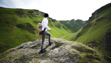 a guitarist standing on top of a mountain and looking down a valley